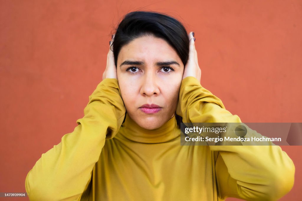 Latino woman looking at the camera and covering her ears, HEAR NO EVIL