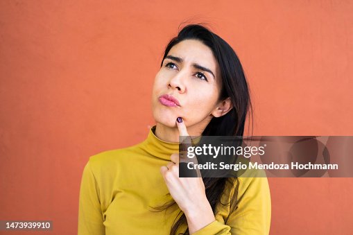 Latino woman deep in thought, thinking and looking up, finger on chin Latino woman deep in thought, thinking and looking up, finger on chin