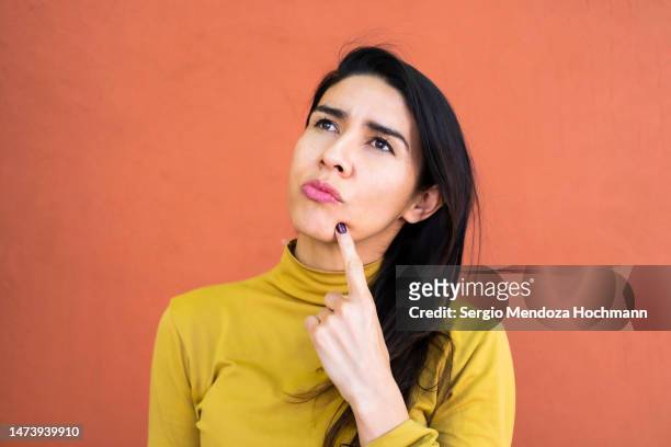 latino woman deep in thought, thinking and looking up, finger on chin - vragen stockfoto's en -beelden