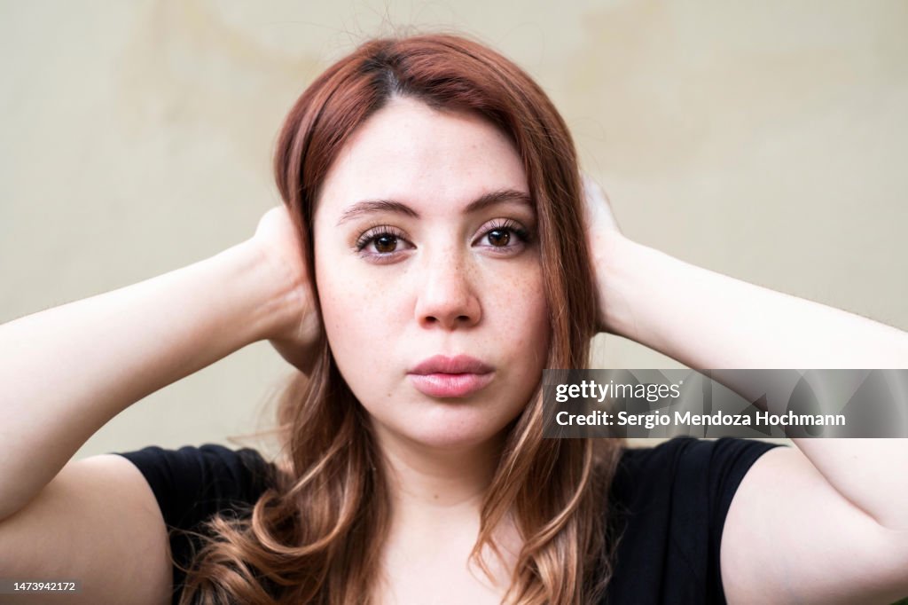 Young caucasian Latino woman looking at the camera and covering her ears, HEAR NO EVIL