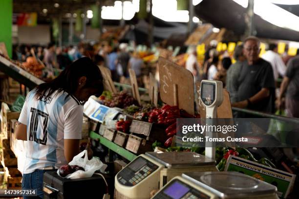 Woman wearing a Lionel Messi Argentine national soccer team jersey weights fruits and vegetables at the Buenos Aires Central Market on March 16, 2023...