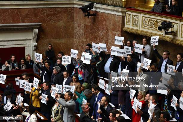 Members of Parliament of left-wing coalition NUPES hold placards as French Prime Minister Elisabeth Borne addresses deputies to confirm the force...