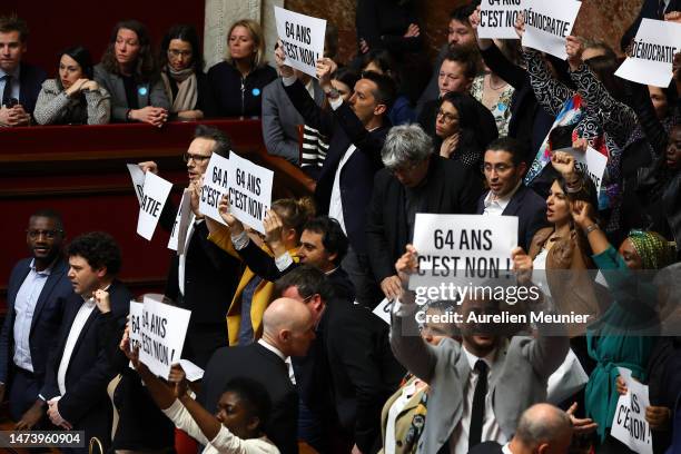 Members of Parliament of left-wing coalition NUPES hold placards as French Prime Minister Elisabeth Borne addresses deputies to confirm the force...