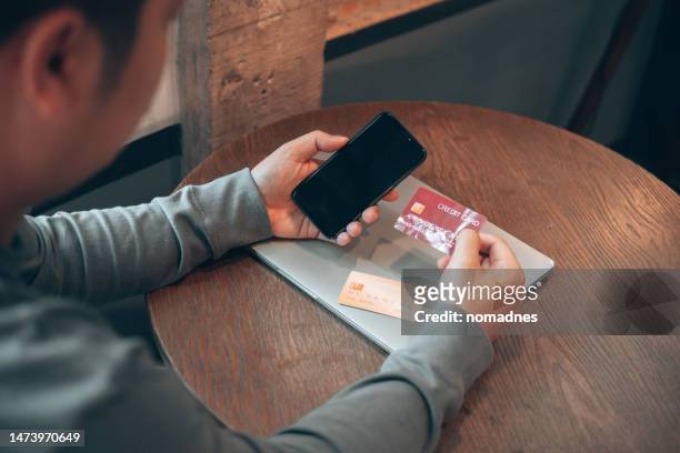 rear view over shoulder, man holding mobile phone and choosing credit card for internet banking. credit card payment for online shopping. concerned for mobile app network security. - lies ストックフォトと画像