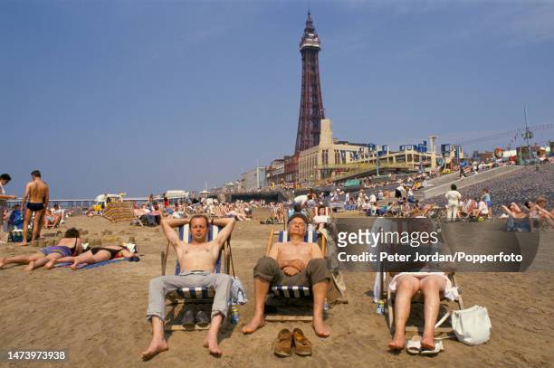 Visitors sunbathing in deckchairs on the beach in the seaside resort town of Blackpool in Lancashire, England in September 1991. Visible in the...