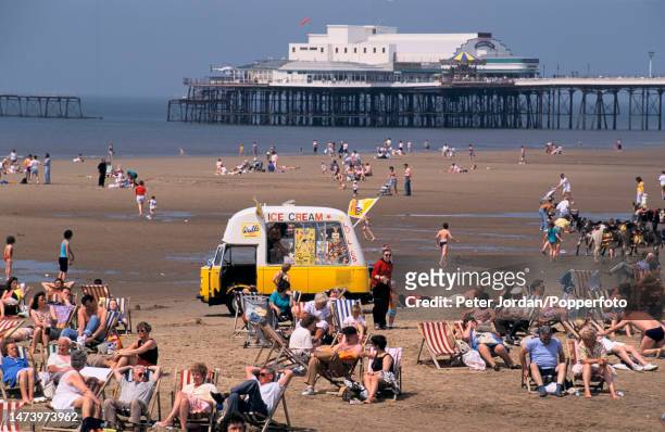 Visitors sunbathe in deckchairs with an ice cream van on the beach in the seaside resort town of Blackpool in Lancashire, England in September 1991.
