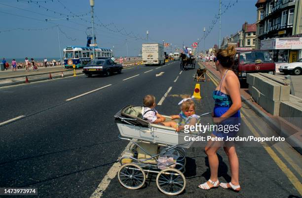 Woman pushes a pram containing two toddlers across the Promenade and Golden Mile in the seaside resort town of Blackpool in Lancashire, England in...