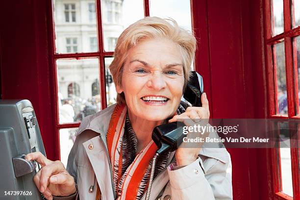 senior woman in red telephone booth. - telefonzelle stock-fotos und bilder