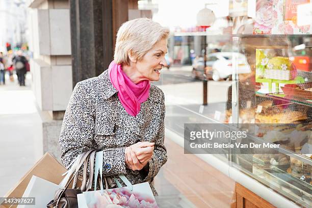 mature woman looking at cakes in window. - désir photos et images de collection