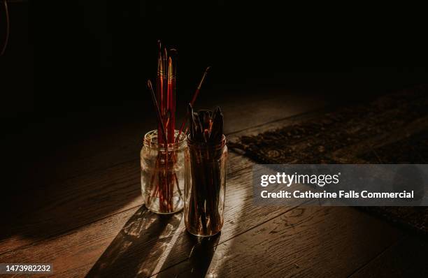 two jam jars containing multiple sized paint brushes - art from the shadows stock pictures, royalty-free photos & images