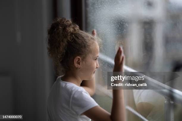 little sad girl pensive looking through the window glass with a lot of raindrops. sadness and loneliness childhood concept image. - girl looking through window stock pictures, royalty-free photos & images