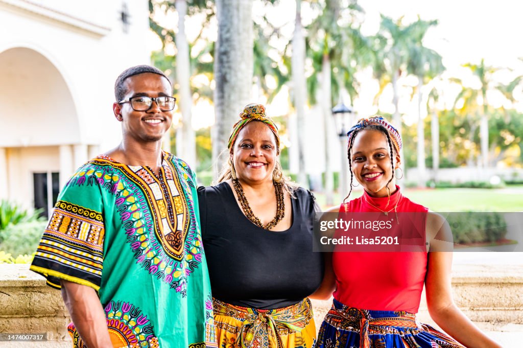 Madre e hijo e hija adultos vestidos con dashiki y ropa tradicional para celebrar Kwanzaa en un retrato familiar feliz al aire libre
