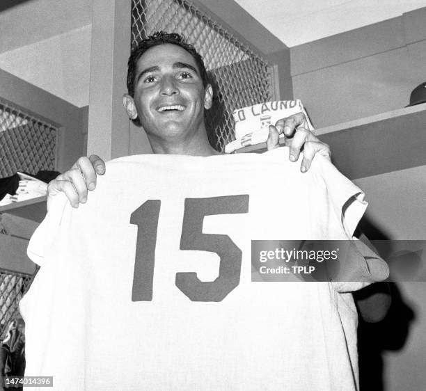 Pitcher Sandy Koufax of the Los Angeles Dodgers holds up teammate Bob Miller's uniform in the locker room after Koufax set a new World Series record...