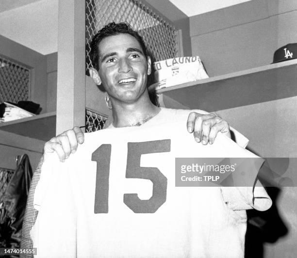 Pitcher Sandy Koufax of the Los Angeles Dodgers holds up teammate Bob Miller's uniform in the locker room after Koufax set a new World Series record...