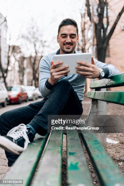 man resting on a bench, holding his tablet - streaming media service stock pictures, royalty-free photos & images