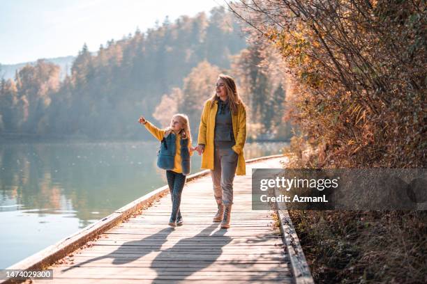 mid adult caucasian woman with her daughter walking around lake bled - herfst stockfoto's en -beelden
