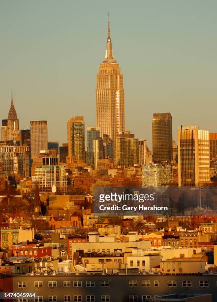 The sun sets on the skyline of midtown Manhattan and the Empire State Building in New York City and homes in Hoboken, New Jersey on March 15 as seen...