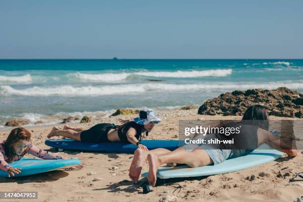 asian surfing enthusiasts are practicing surfing on the beach, with the guidance of a coach who is ensuring the accuracy and details of their movements. - exercise instructor stock pictures, royalty-free photos & images