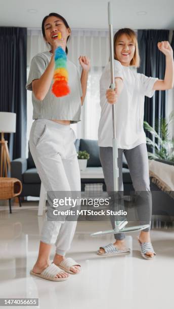young asian lesbian couples having fun during cleaning house and singing with mop live online screen ig reel tiktok at living room. dancing and singing in a cozy room. vertical screen. - the sound of change live stock pictures, royalty-free photos & images