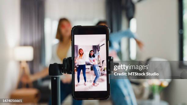 young asian lesbian couples influencer having fun dancing trendy music together live online screen ig reel tiktok in living room at home. dancing and singing in a cozy room. - funny lesbian 個照片及圖片檔