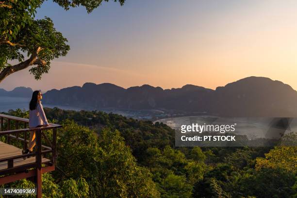 a woman standing at phi phi view point and see the view from a bird's eye view of the mountains, the sea and the sunset. and town on phi phi island, krabi province, thailand - travel stock-fotos und bilder
