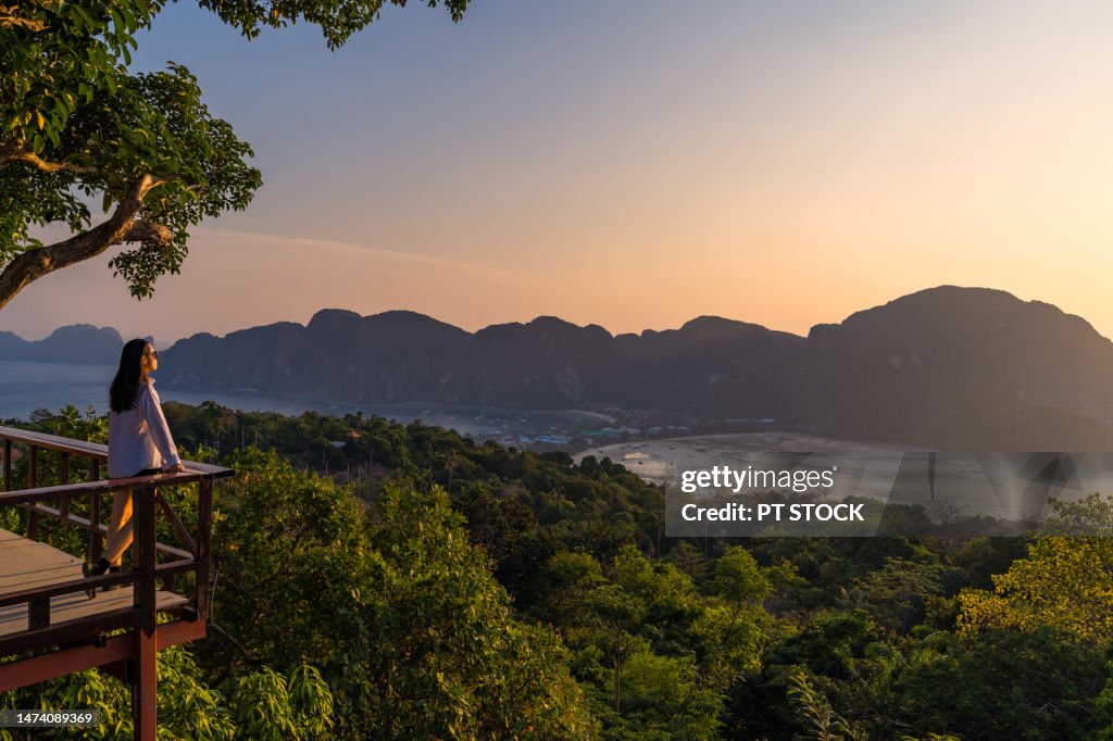 A woman standing at Phi Phi View Point And see the view from a bird's eye view of the mountains, the sea and the sunset. and town on Phi Phi Island, Krabi Province, Thailand