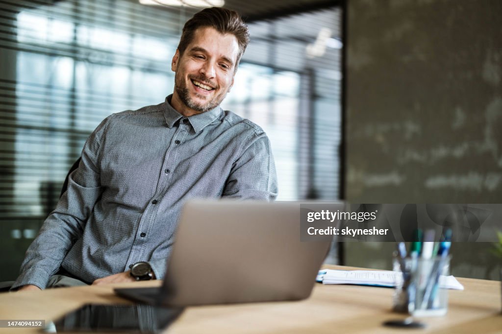 Happy businessman reading an e-mail on laptop in the office.