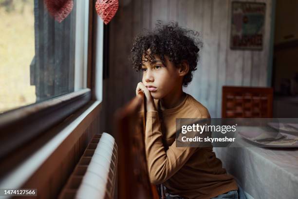 sad black boy looking through window from home. - alleen één jongen stockfoto's en -beelden