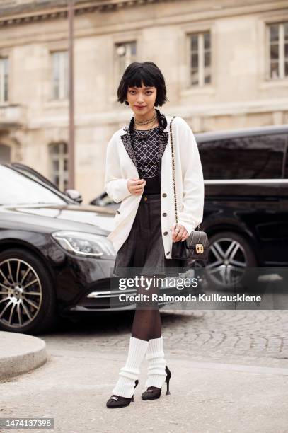 Chau Bui wears a Chanel top, black leather mini skirt, white cardigan, white leg warmers, and Chanel bag and shoes, outside the Chanel show during...