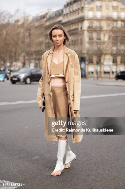 Nataly Osmann wears a beige Miu Miu crop top with matching midi skirt, beige denim coat outside the Miu Miu show during Paris Fashion Week F/W 2023...