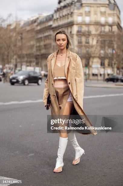 Nataly Osmann wears a beige Miu Miu crop top with matching midi skirt, beige denim coat outside the Miu Miu show during Paris Fashion Week F/W 2023...