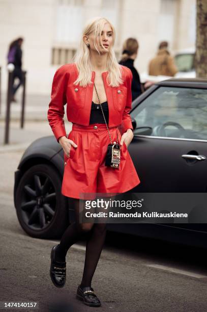 Xenia Adonts seen wearing a red leather set with a jacket and shorts, a black top, black transparent tights, black loaders and a jukebox bag outside...