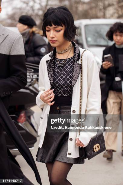 Chau Bui wears a Chanel top, black leather mini skirt, white cardigan, white leg warmers, and Chanel bag and shoes, outside the Chanel show during...