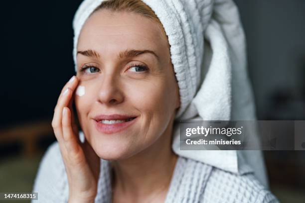 nahaufnahme einer lächelnden frau, die morgens feuchtigkeitscreme aufträgt - gesichtscreme stock-fotos und bilder