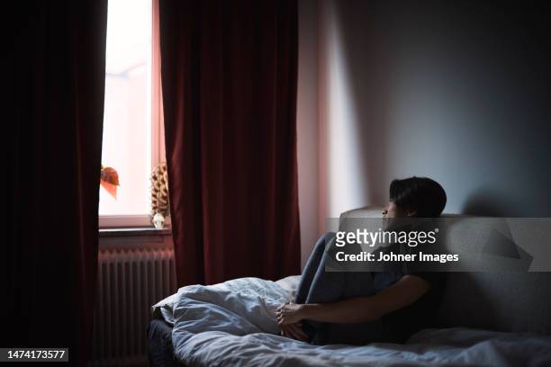 pensive man sitting on sofa and looking through window - eenzaamheid stockfoto's en -beelden