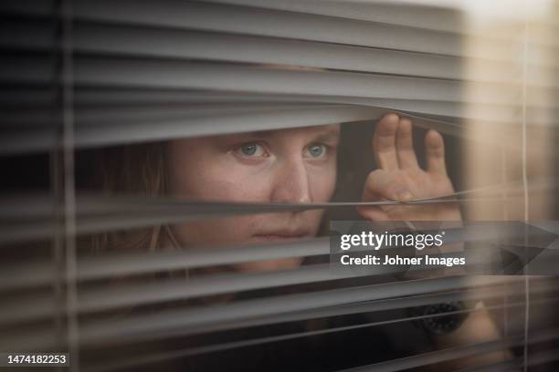 blond man peeking through window blinds - hypochondria stock pictures, royalty-free photos & images