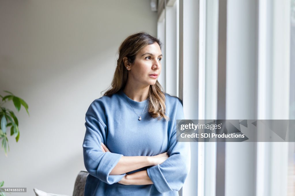 Serious businesswoman with arms crossed looks out office window