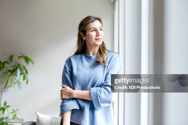 ama de casa mira por la ventana y sueña despierta - adulto de mediana edad fotografías e imágenes de stock