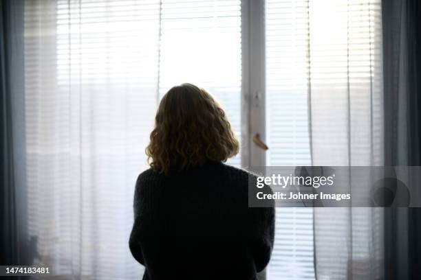 rear view of teenage girl looking through window - back stock pictures, royalty-free photos & images