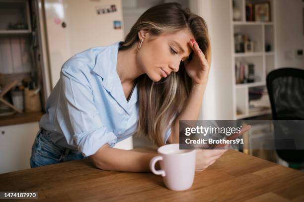 young woman using her cellphone while drinking coffee in kitchen - 垃圾郵件 電子郵件 個照片及圖片檔