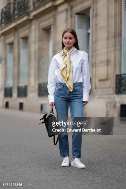 Diane Batoukina wears a white oversize shirt, a pastel yellow scarf from Hermes, a black leather bag from Hermes, blue jeans , during a street style...