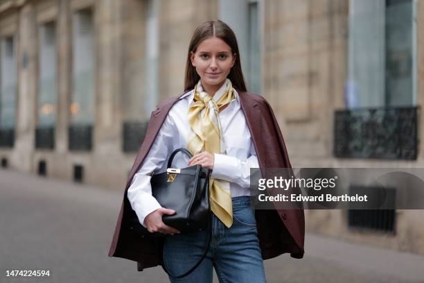 Diane Batoukina wears a white oversize shirt, a pastel yellow scarf from Hermes, a burgundy leather blazer jacket, a black leather bag from Hermes,...