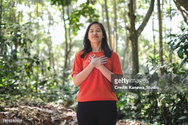 jeune femme asiatique méditant dans la nature - main sur la poitrine photos et images de collection