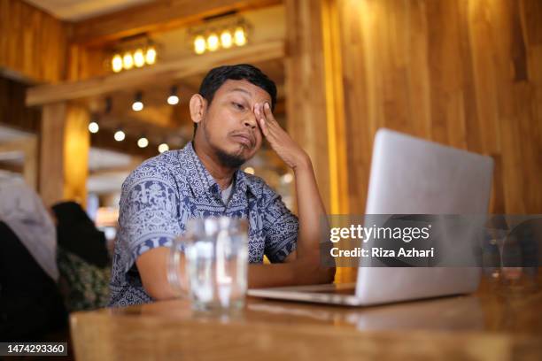 hombre asiático que tiene dolor en los ojos mientras trabaja en una cafetería - bloodshot fotografías e imágenes de stock