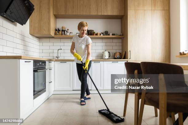 la donna matura lava il pavimento in cucina usando un mocio - cameriera foto e immagini stock