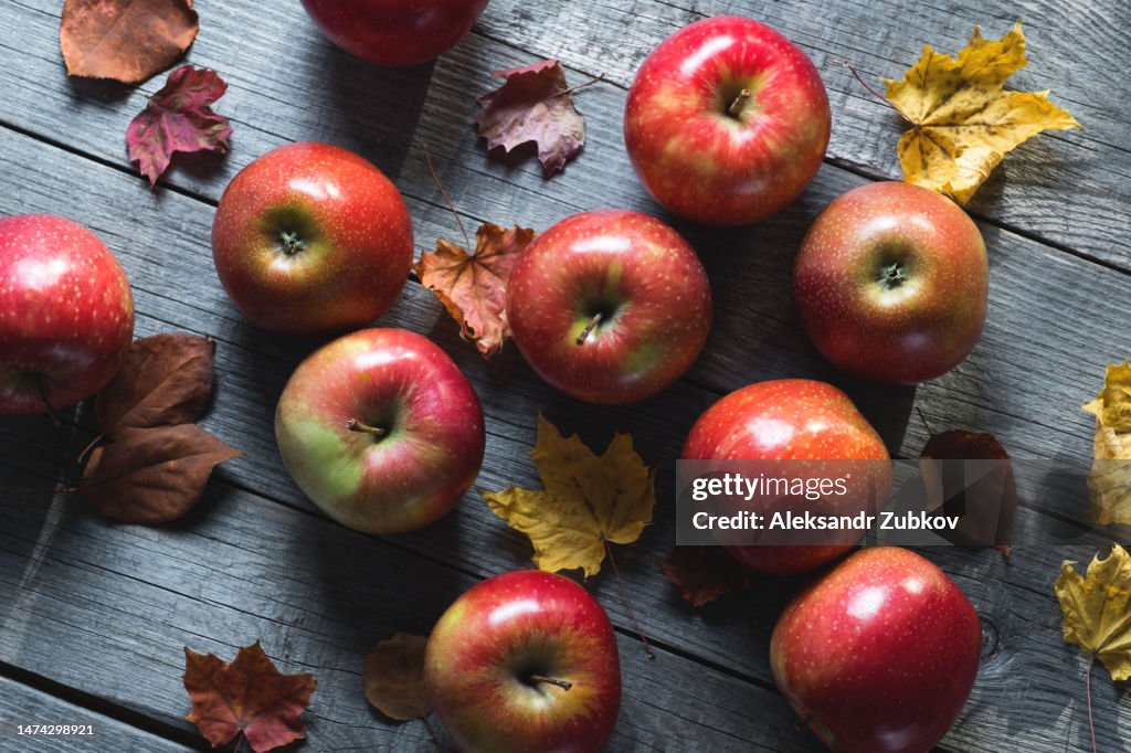 Red apples and fallen yellow autumn leaves of birch, maple and aspen on a wooden background. Fruit on the kitchen table. Cultivation of organic farm products. The concept of vegetarian, vegan, raw food and diet. Autumn natural background. Harvesting.