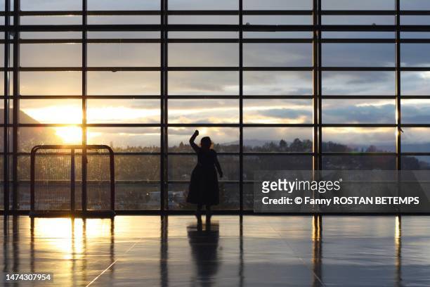a little girl is dancing in her princess dress in a large empty theater, a glass wall and the sunset in the background - watching sunset stock pictures, royalty-free photos & images