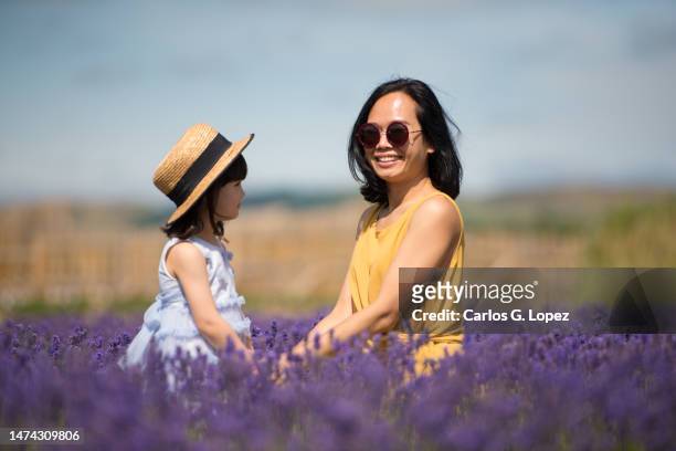 a young asian mother wearing a yellow jumpsuit dress an sunglasses holds hands with her daughter while sitting in the middle of a lavender field in a sunny summer day in kinross, scotland, uk - level 5 stock pictures, royalty-free photos & images