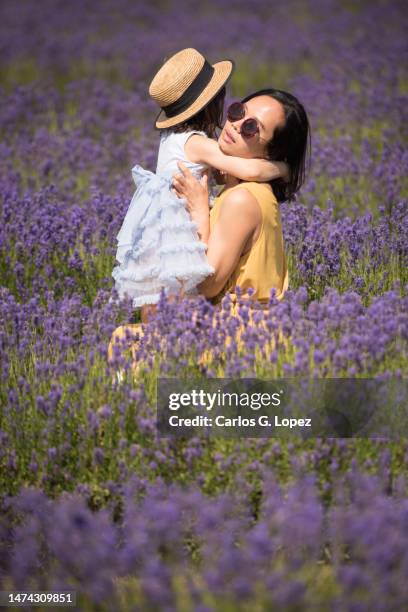 young asian mother wearing a yellow jumpsuit dress an sunglasses cuddling her daughter while sitting in the middle of a lavender field in a sunny summer day in kinross, scotland, uk - girls jumpsuit stock pictures, royalty-free photos & images