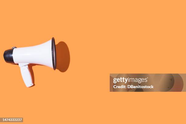 white megaphone with black trim on an orange background. scream, message, announcement and news concept. - horn press stock pictures, royalty-free photos & images